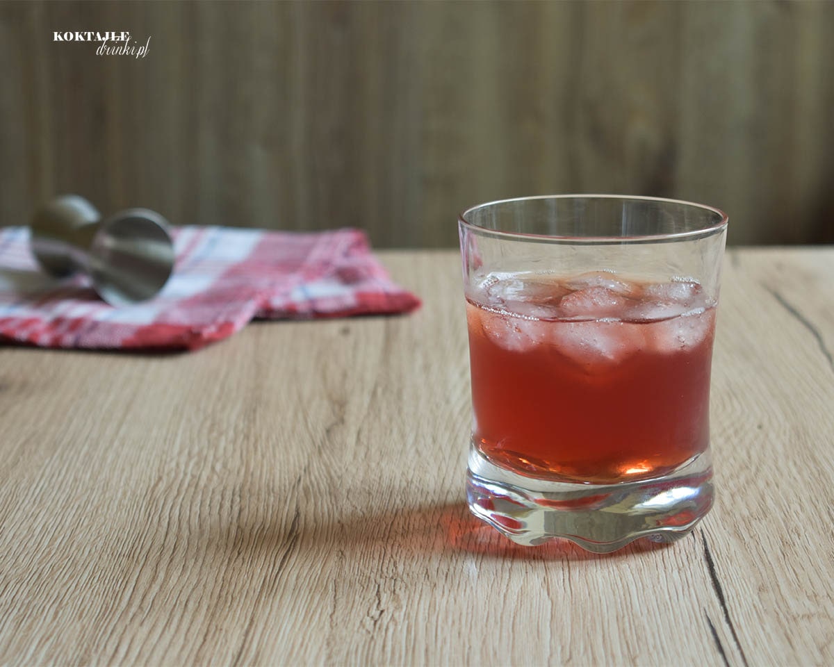 Drink Bloody Whisky w niskiej szklance o barwie jasno czerwonej z kostkami lodu.