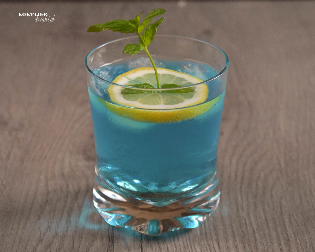Drugie ujęcie na błękitny drink Blue Gin od frontu, widać plasterek cytryny i gałązkę mięty wystająca znad szklanki.
