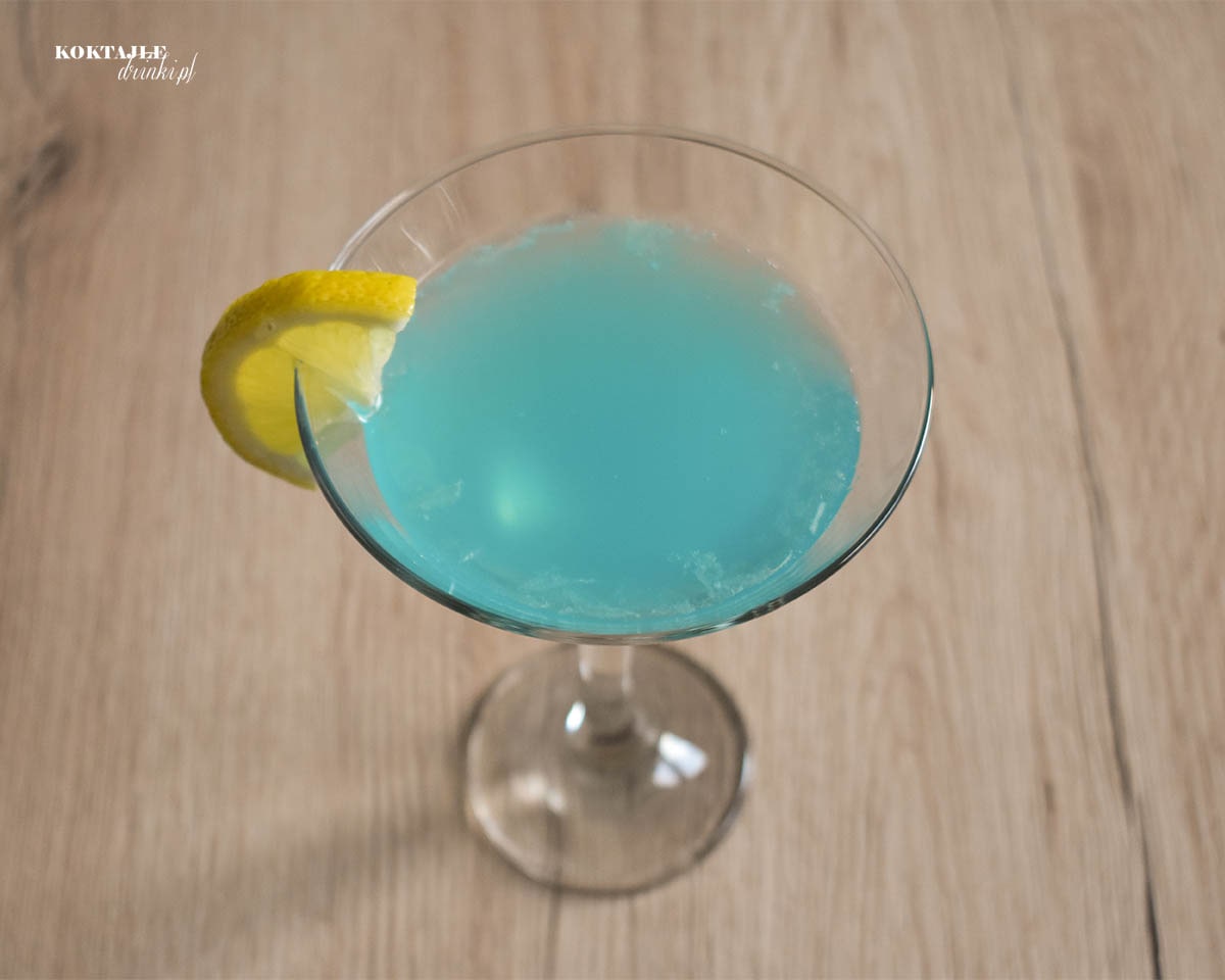 Widok z góry na drink z ginem, Blue Lady o błękitnej barwie w kieliszku ozdobionym kawałkiem cytryny.