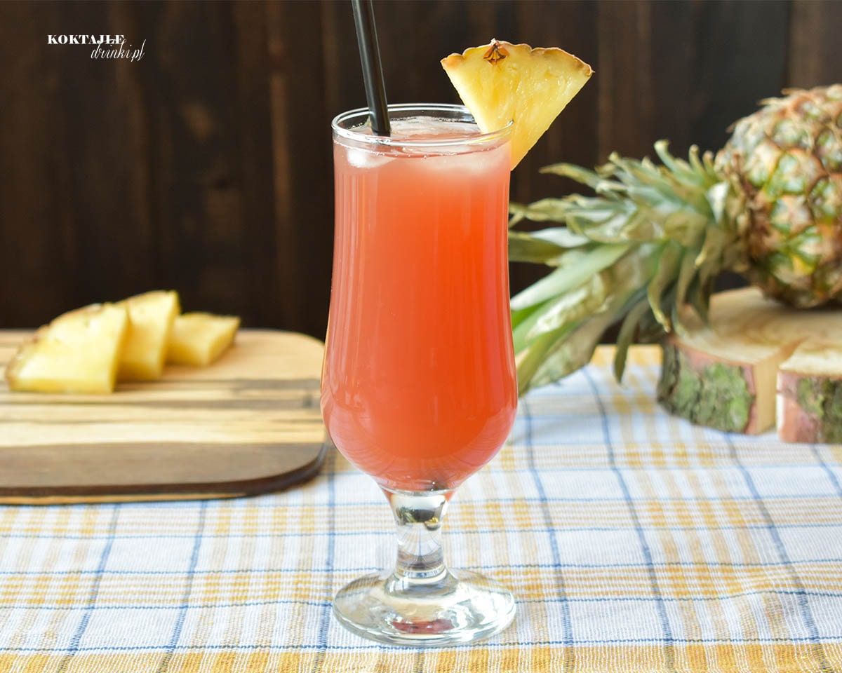 Drink z wódką Burnso Tropical jasno czerwony w szklance ozdobionej ananasem.