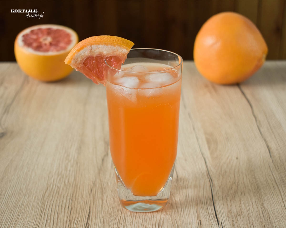 Drink z aperol, Grape Wild Aperol, o pomarańczowej barwie w wysokiej szklance ozdobionej kawałkiem grejpfruta.