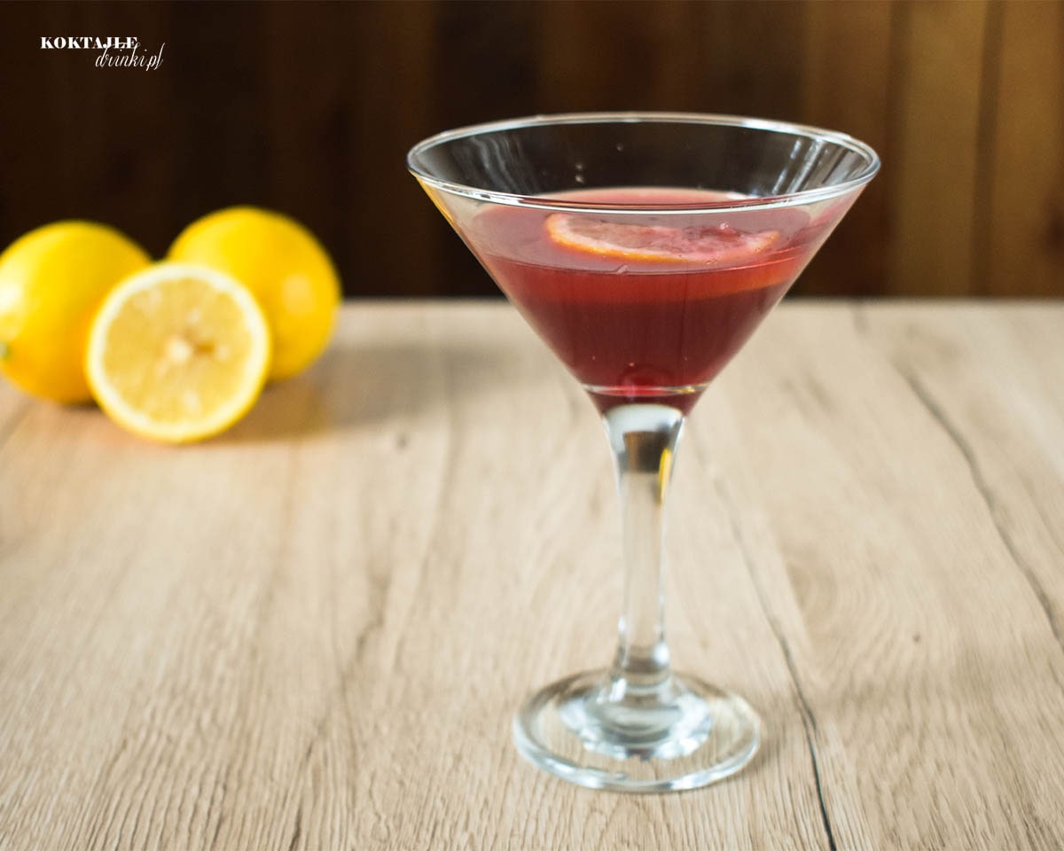 Drink Red Jager Sour w kieliszku koktajlowym o barwie czerwonej w otoczeniu cytryn.