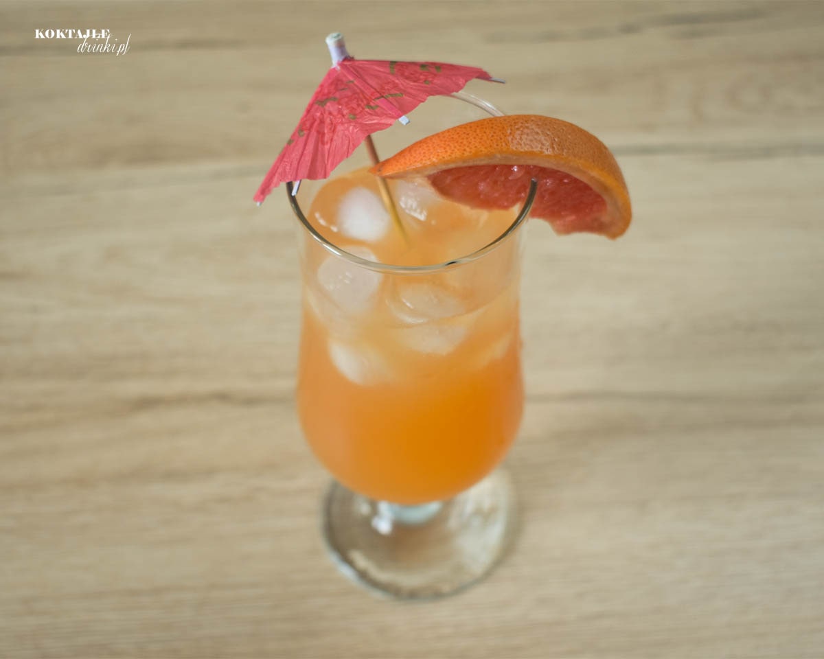 Ujęcie z góry na drink Słoneczne Orzeźwienie, zbliżenie na parasolkę i kawałek grejpfruta.