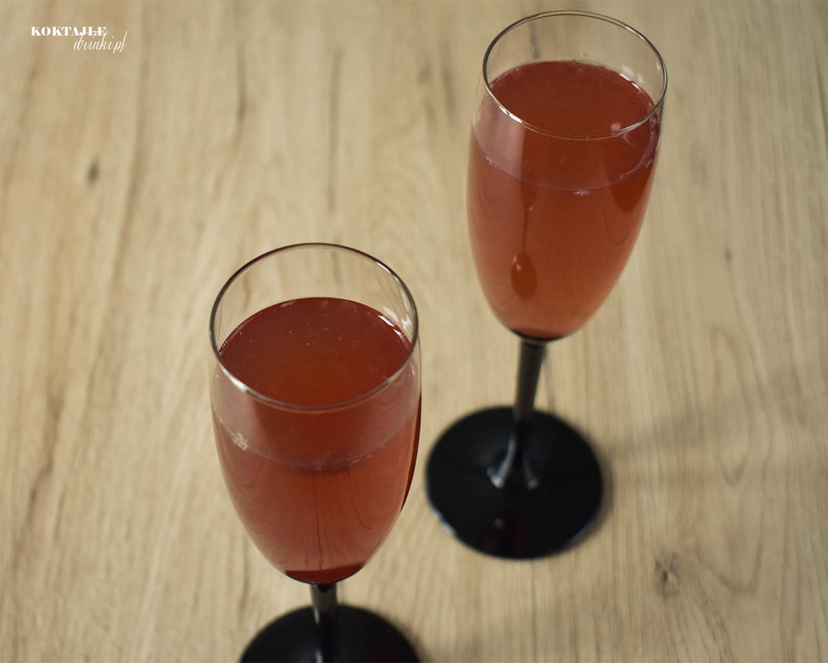 Ujęcie z góry na drink z szampanem prosecco i malibu, widoczne 2 musujące jasno czerwone kieliszki.