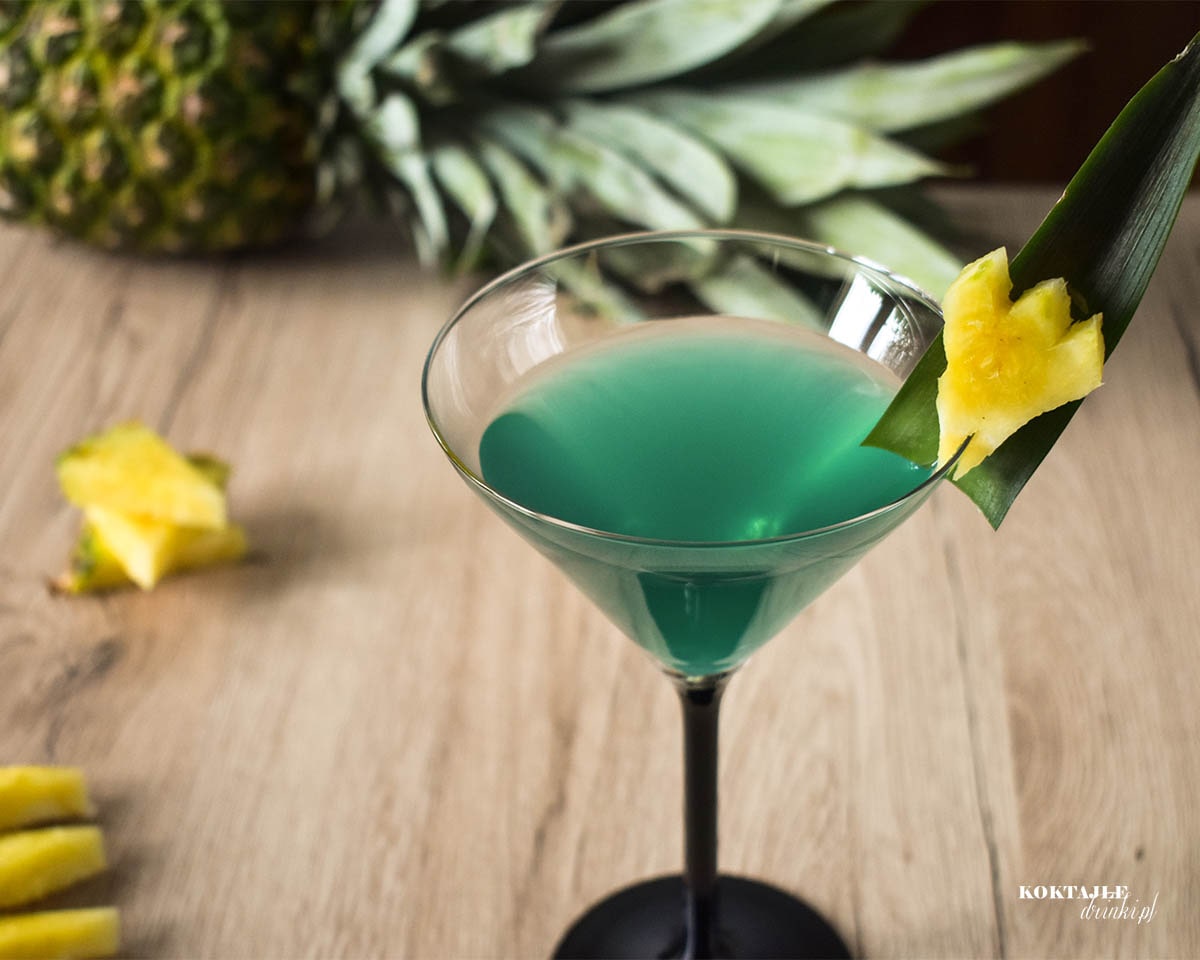 Drink z malibu o zielonej barwie w kieliszku ozdobionym kawałkiem ananasa.