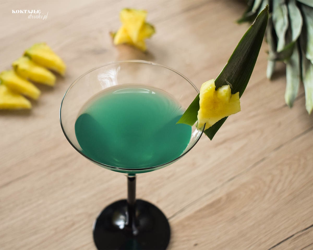 Zielony drink z malibu w ujęciu drugim z góry, zbliżenie na liść ananasa wraz z jego kawałkiem.