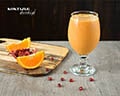 Koktajl owocowy smoothie o barwie pomarańczowej w otoczeniu ćwiartek pomarańczy i pestek granatu.