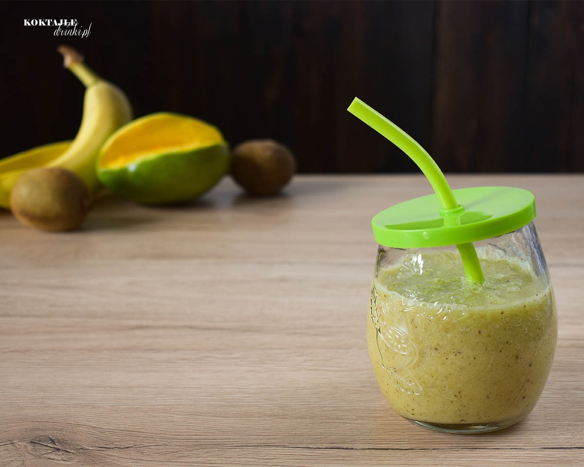 Koktajl owocowy smoothie o barwie zielonej, w tle widoczne banany, kiwi oraz mango.